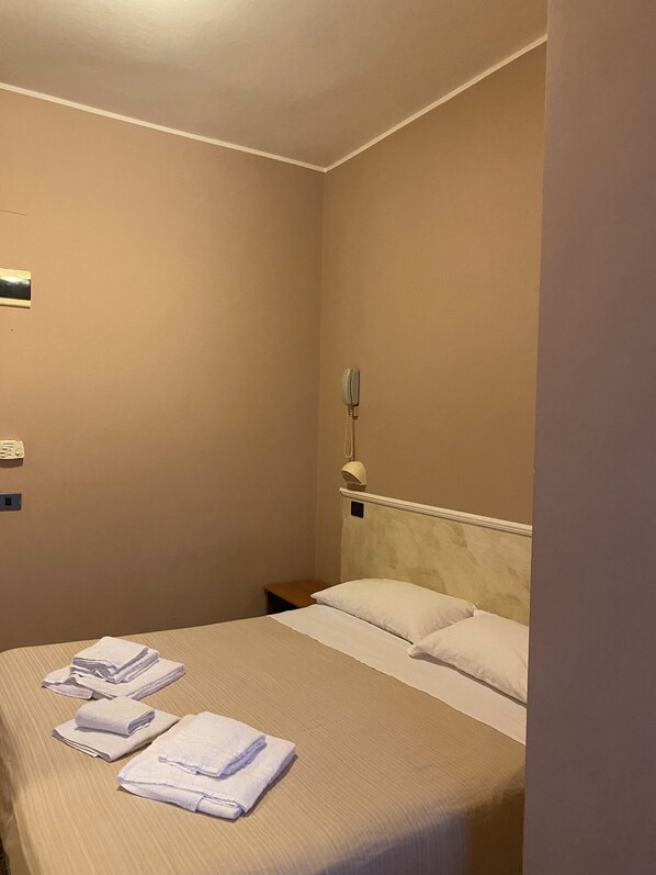 A hotel room with a neatly made bed, a bedside telephone, and a small bedside table. - Viale Lazzaro Papi (Rimini)