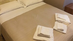 A neatly made bed with white linens and towels, a headboard, and a small bedside table. - Viale Lazzaro Papi (Rimini)
