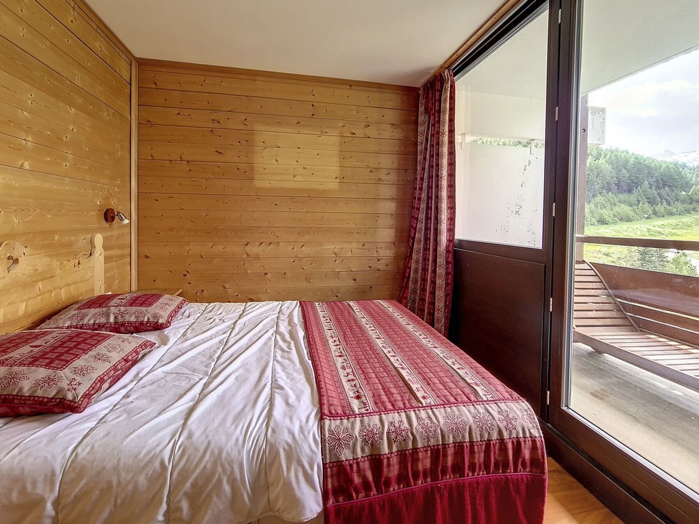 A wooden-paneled room with a bed, a window, and a view of greenery.