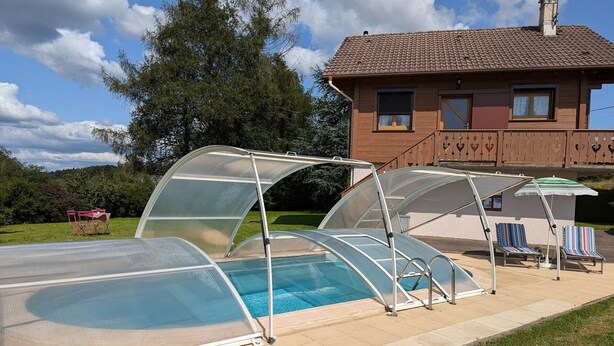 En swimmingpool med et glaslaug, et overdækket opholdsområde med liggestole, og et hus i baggrunden.