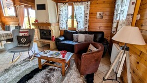 Indbydende interiør i en hytte med pejs, trævægge, sofa, gyngestol og spiseplads.