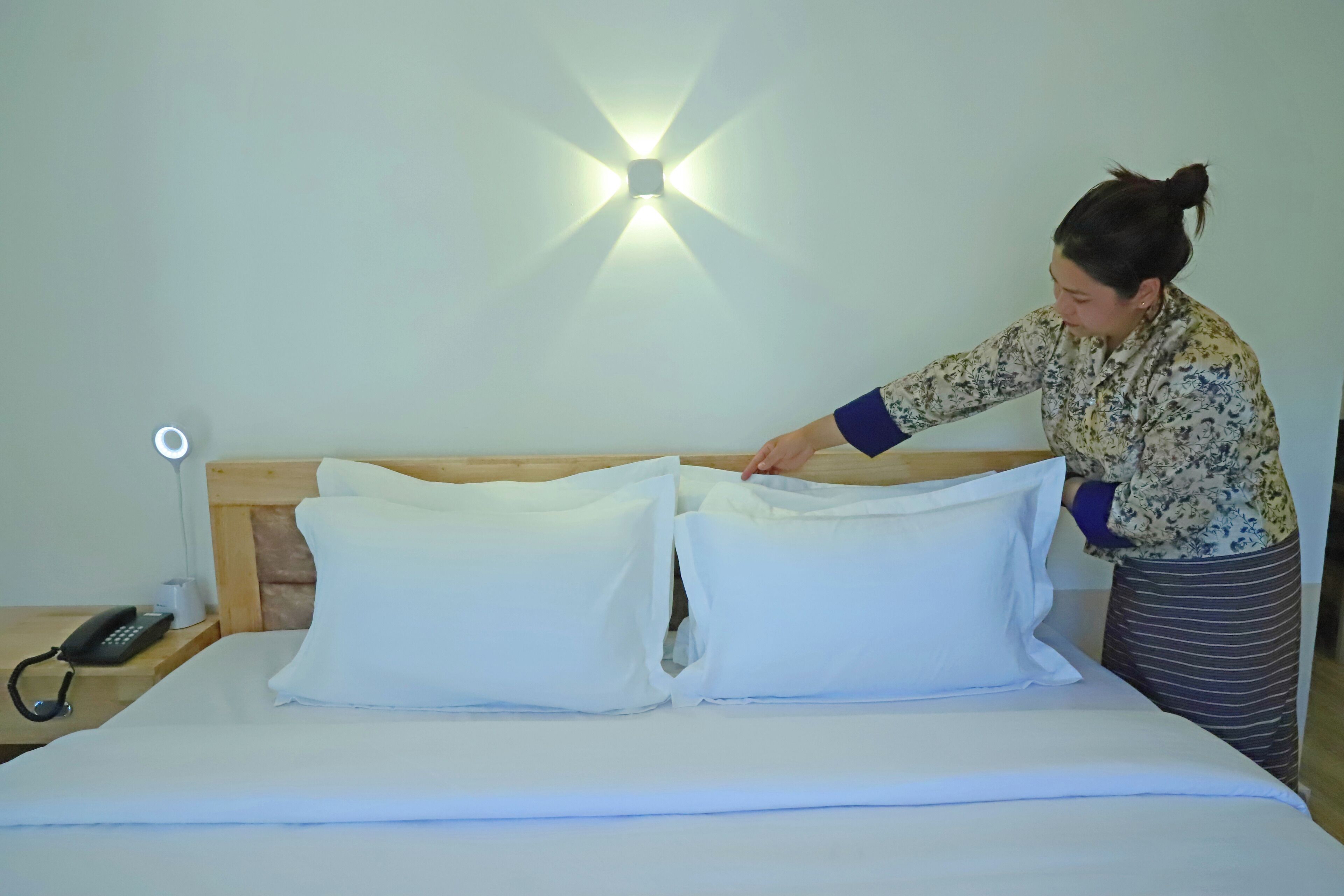A neatly made bed with white linens and pillows, a bedside lamp, and a phone on the nightstand.