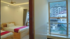 A hotel room with two beds, a ceiling fan, and a window with a view of buildings. - The BD Hotel (Thimphu)