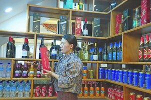 Uma pessoa vestindo camisa estampada olhando prateleiras repletas de diversas bebidas, incluindo vinho e latas.