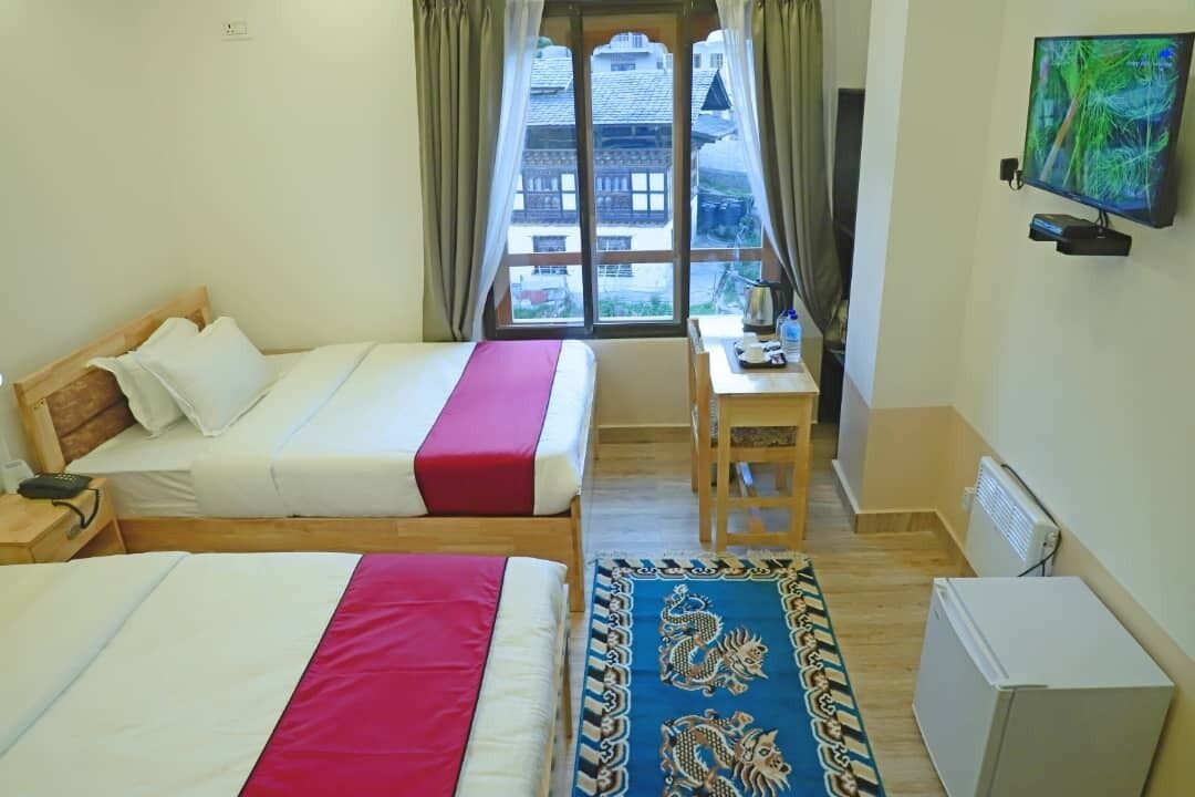 Habitación de hotel con dos camas, un escritorio, un televisor y una ventana con vista a edificios.