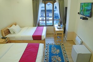 Quarto de hotel com duas camas, uma escrivaninha, televisão e janela com vista para edifícios.
