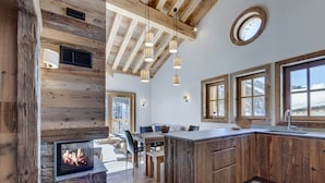 A rustic kitchen with a stone fireplace, wooden beams, and large windows.