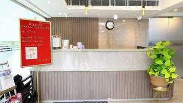 A hotel reception area with a red welcome sign, a clock, and a plant.