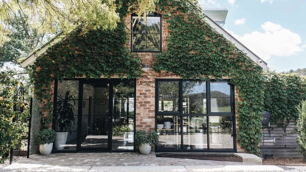 A house with a brick exterior partially covered in ivy, large glass windows, and potted plants in front.