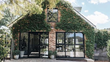 A house with a brick exterior partially covered in ivy, large glass windows, and potted plants in front.