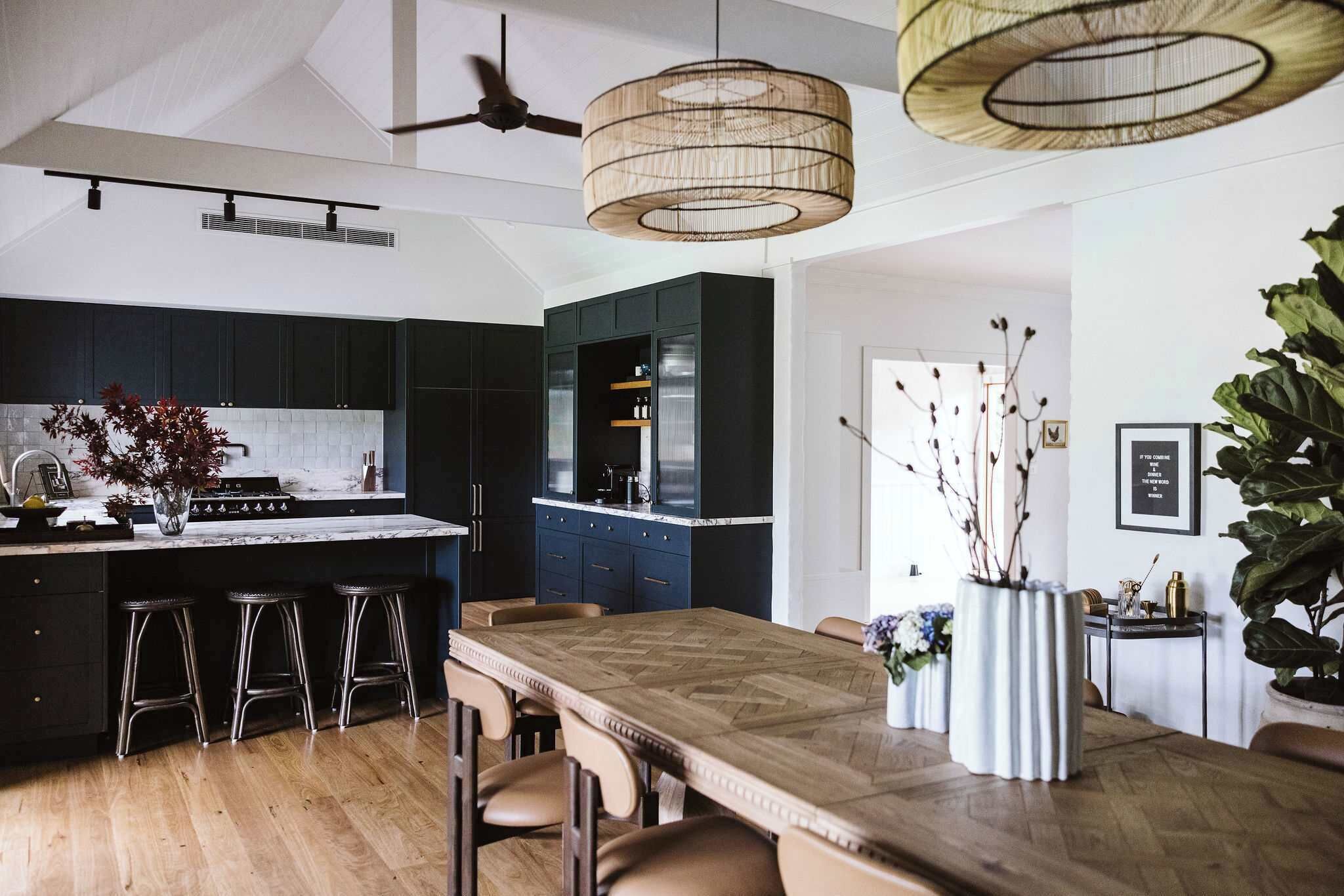 A modern kitchen with dark cabinets, a wooden dining table, and bar stools.