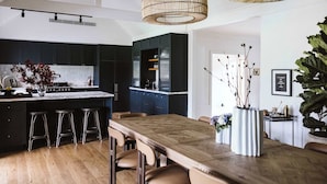 A modern kitchen with dark cabinets, a wooden dining table, and bar stools.