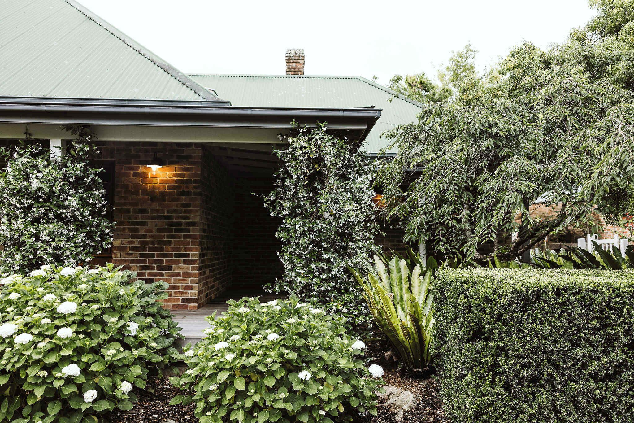 A house with a brick entrance, a well-maintained garden with various plants, and a visible chimney.