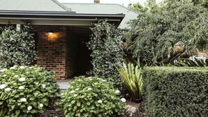 A house with a brick entrance, a well-maintained garden with various plants, and a visible chimney.