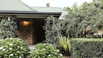 A house with a brick entrance, a well-maintained garden with various plants, and a visible chimney.