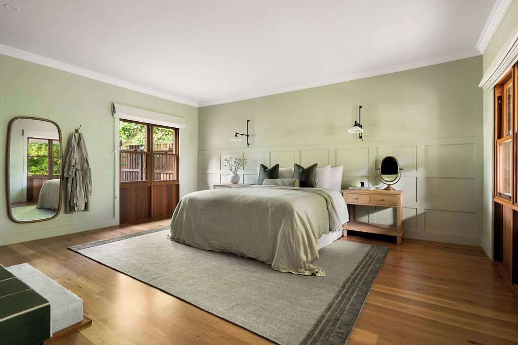 A bedroom with a bed, bedside table, mirror, and a view of the outside.