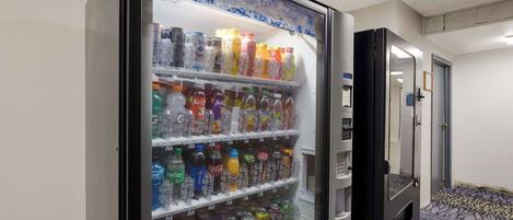 Máquina expendedora llena de diversas bebidas en un pasillo de hotel.