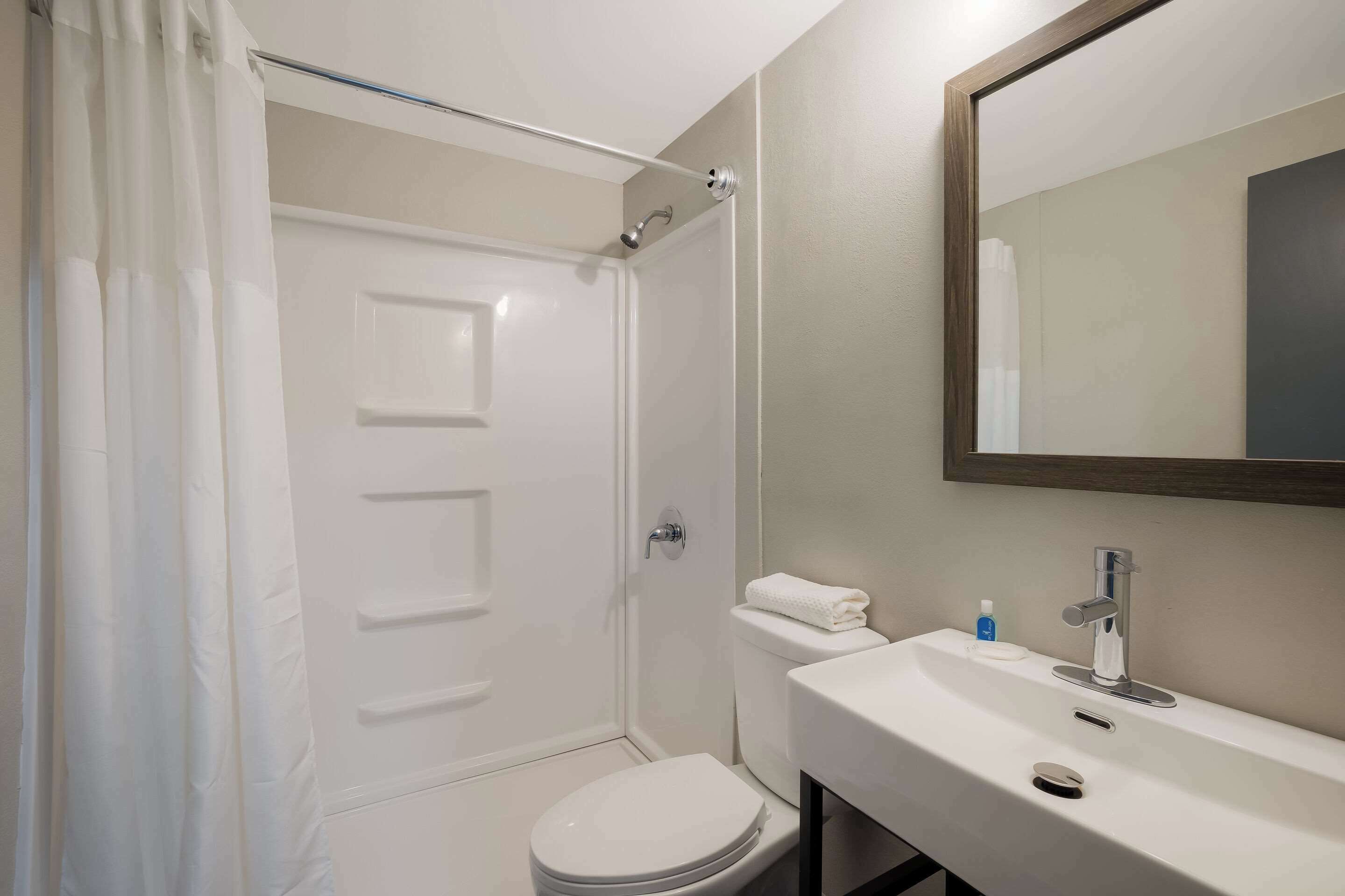 Un baño con inodoro blanco, lavabo con espejo y zona de ducha.