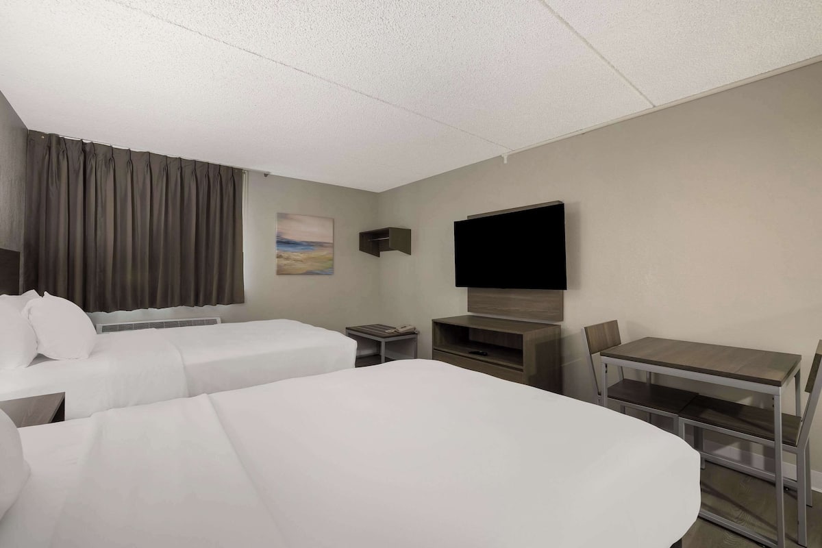 Ett hotellrum med två sängar, ett skrivbord, en stol, en TV och en liten hylla.