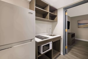 Una cucina moderna con forno a microonde integrato, lavello e piano cottura. Si vedono mensole in legno sopra il bancone e un mobile sottostante.
