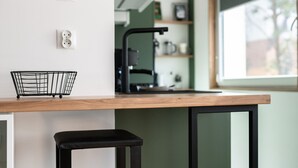 A kitchen area with a wooden countertop, a black stool, a black metal wire basket, and a black faucet. - Cozy Apartment in a quiet area | Washing machine | Close to the Park (Poznan)
