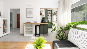 A modern living room with a sofa, a coffee table, and a potted plant. There is a kitchen area with a counter and cabinets. - Cozy Apartment in a quiet area | Washing machine | Close to the Park (Poznan)