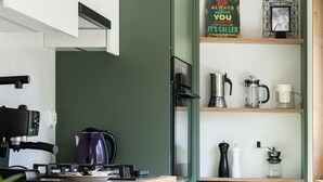 A modern kitchen with a gas stove, a kettle, and a coffee maker on the counter. There are shelves above the counter holding decorative items and kitchenware. - Cozy Apartment in a quiet area | Washing machine | Close to the Park (Poznan)