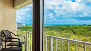 A balcony with wicker chairs, a view of a building across the water, and a tropical landscape. - Key Largo Baha Penthouse Ocean Pointe 1416 (Tavernier)