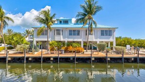A two-story house with a blue roof, white walls, and a dock extending into a body of water. - Key Largo Baha Penthouse Ocean Pointe 1416 (Tavernier)