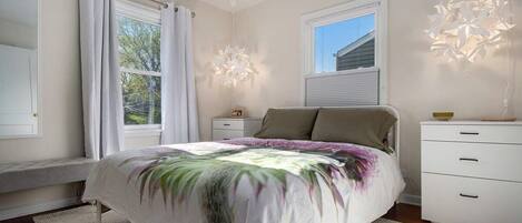 Une chambre à coucher comprenant un lit, une table de chevet, une commode et une fenêtre avec des rideaux.