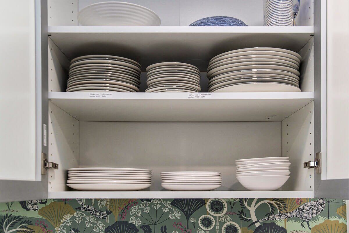 A kitchen cabinet with multiple shelves holding stacks of plates and bowls.