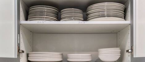 A kitchen cabinet with multiple shelves holding stacks of plates and bowls.