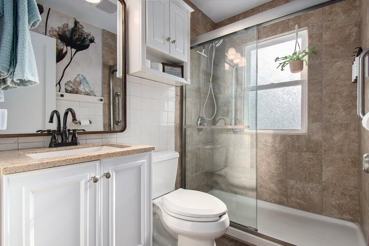 A modern bathroom with a glass-enclosed shower, a white toilet, and a vanity with a mirror.