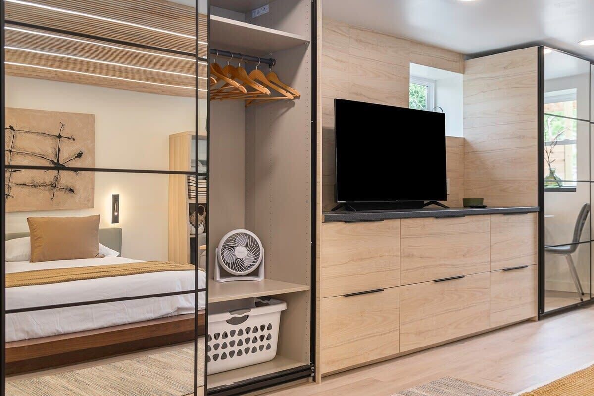 Une chambre moderne équipée d’un lit, d’une télévision, d’un ventilateur et d’une armoire avec un miroir.