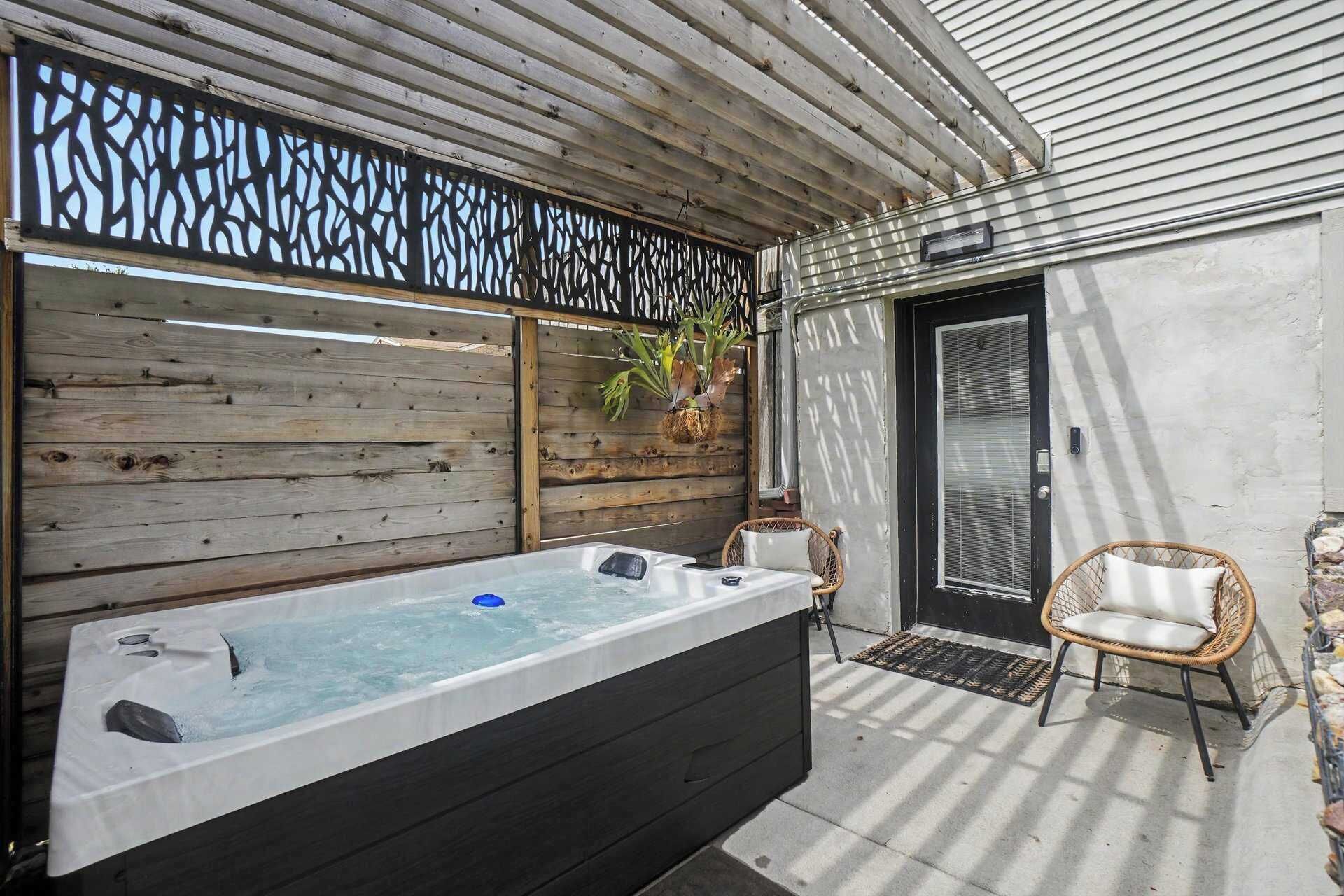Un área de spa con un jacuzzi, sillas de mimbre y una pared de madera con un panel decorativo.