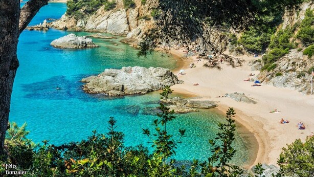 Een kuststrand met helder turquoise water, rotsformaties en een zandstrand.