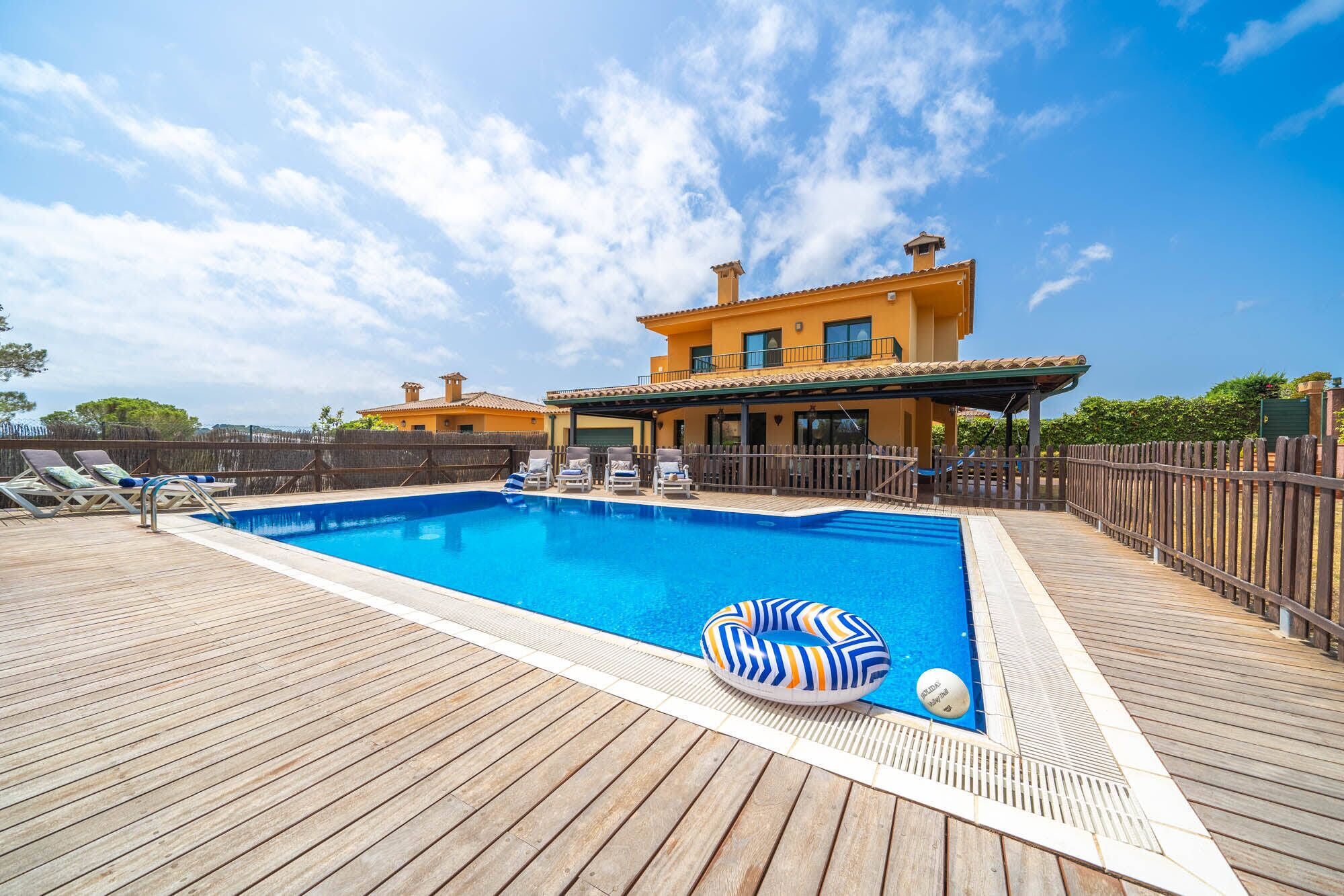 A swimming pool with wooden deck, lounge chairs, and a house in the background.