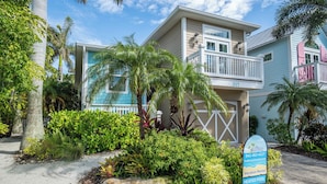 A two-story house with a balcony, surrounded by tropical vegetation and a sign advertising vacation rental with a heated pool. - Pool - Beach Bellini by SeaBreeze Vacation (Holmes Beach)