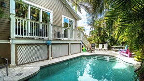 A swimming pool with a wooden deck and a covered area with chairs and a table. - Pool - Beach Bellini by SeaBreeze Vacation (Holmes Beach)