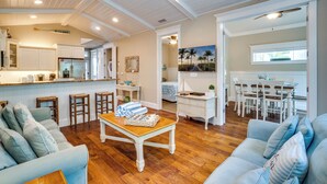 A spacious living area with a wooden floor, a dining table, and a kitchen in the background. - Pool - Beach Bellini by SeaBreeze Vacation (Holmes Beach)