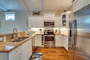 A kitchen with white cabinets, stainless steel appliances, a granite countertop, and a wooden floor.