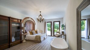 Een ruime slaapkamer met een groot bed, een hangstoel, een badkuip en uitzicht op groen.