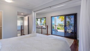 A bedroom with a large bed, a balcony with a view of the ocean, and a sliding glass door leading to an outdoor area. - Beautifully Renovated Large Home on Lammermoor Beach. (Yeppoon)