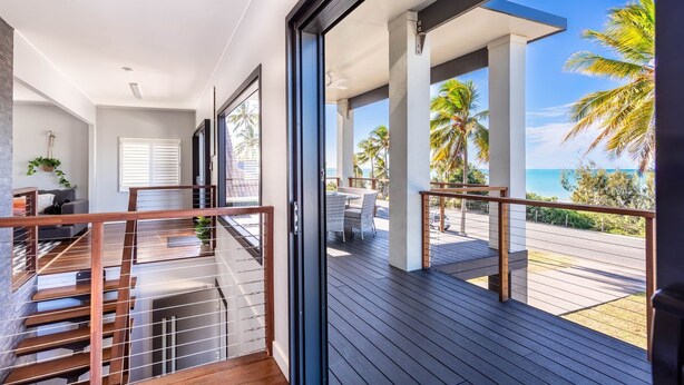 A modern balcony with wooden flooring and metal railings, overlooking a beach with palm trees and the ocean. - Beautifully Renovated Large Home on Lammermoor Beach. (Yeppoon)
