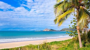A beach with clear blue water, a sandy shore, and a palm tree. - Beautifully Renovated Large Home on Lammermoor Beach. (Yeppoon)