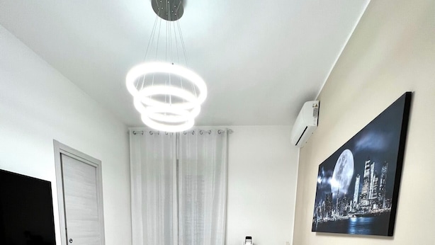 Un dormitorio moderno con una cama curva, un televisor montado, un cuadro de un paisaje urbano y una lámpara en el techo.
