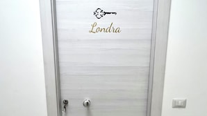 Una puerta cerrada con una mirilla y cerradura, una placa con el nombre 'Londra', y un interruptor de luz en la pared a la derecha.