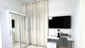 Un dormitorio moderno con armario, escritorio con silla, televisor de pantalla plana y equipo de aire acondicionado.