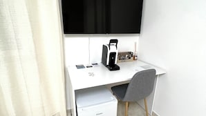 Un espacio de oficina moderno con un escritorio blanco, un televisor de pantalla plana grande, un refrigerador blanco pequeño y una silla gris.