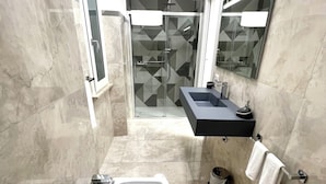 Un baño moderno con un lavabo grande, una cabina de ducha de vidrio y un espejo sobre el lavabo.
